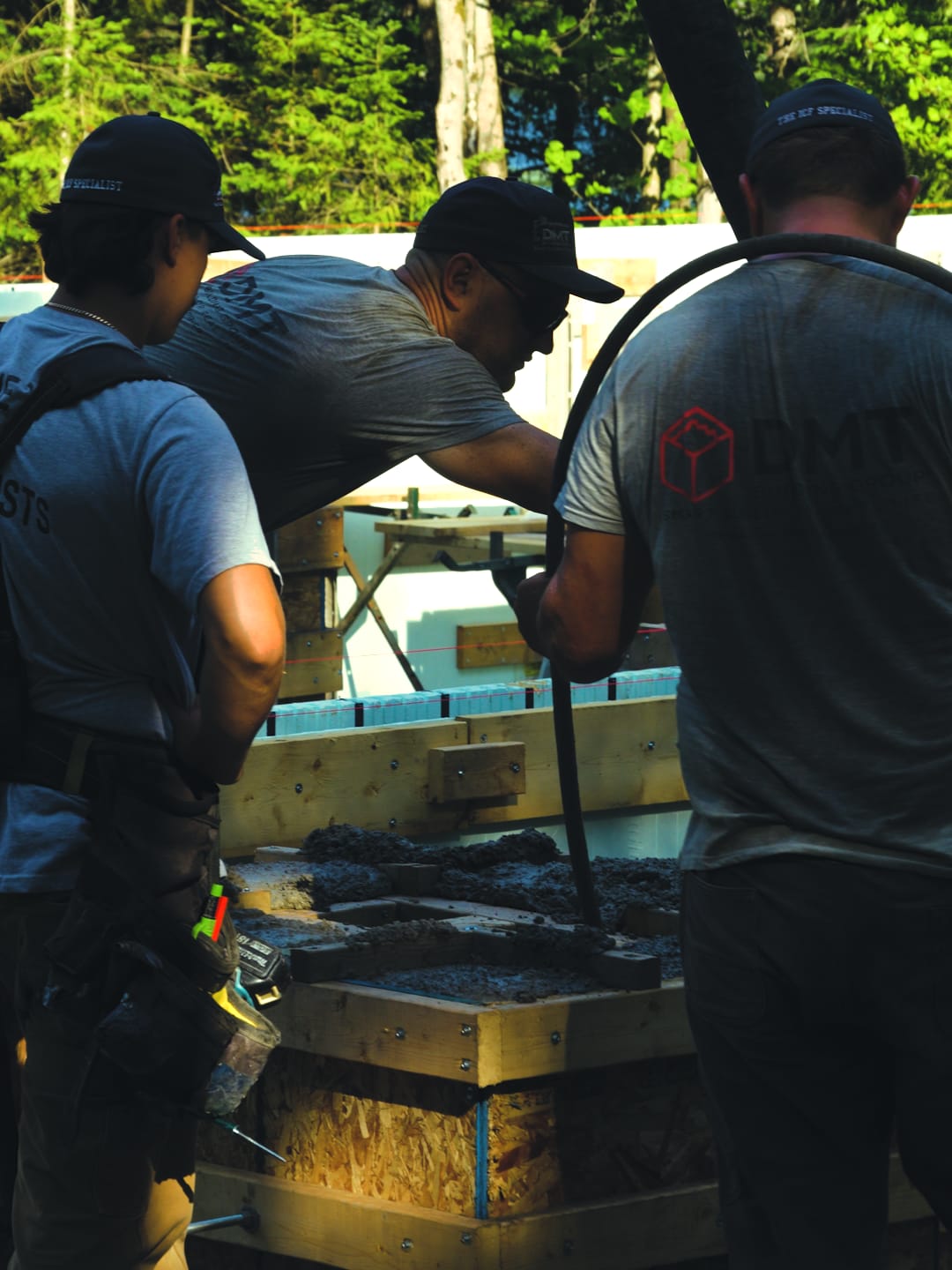 Three DMT crew members working over a column form as fresh concrete goes in during an ICF pour