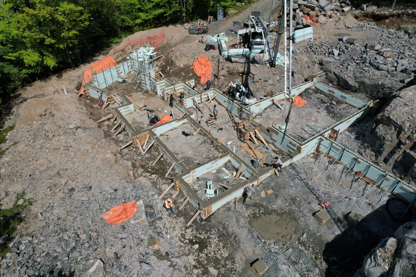 Aerial view of Nudura ICF foundation walls stepping across exposed granite, braced and being filled by a concrete pump boom