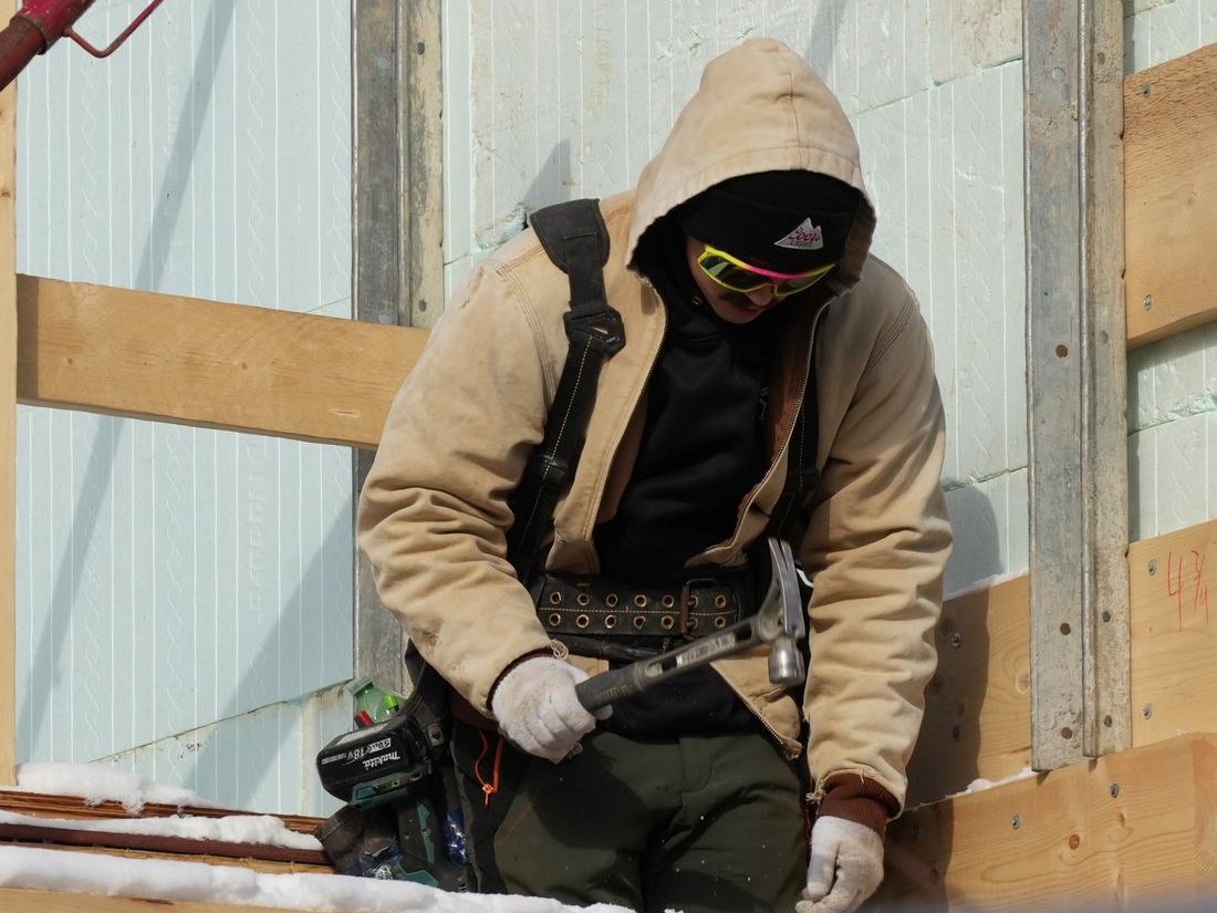 A crew member in a hooded jacket and safety glasses detailing a braced ICF wall in cold weather, the crew skill behind most insulated concrete forms disadvantages
